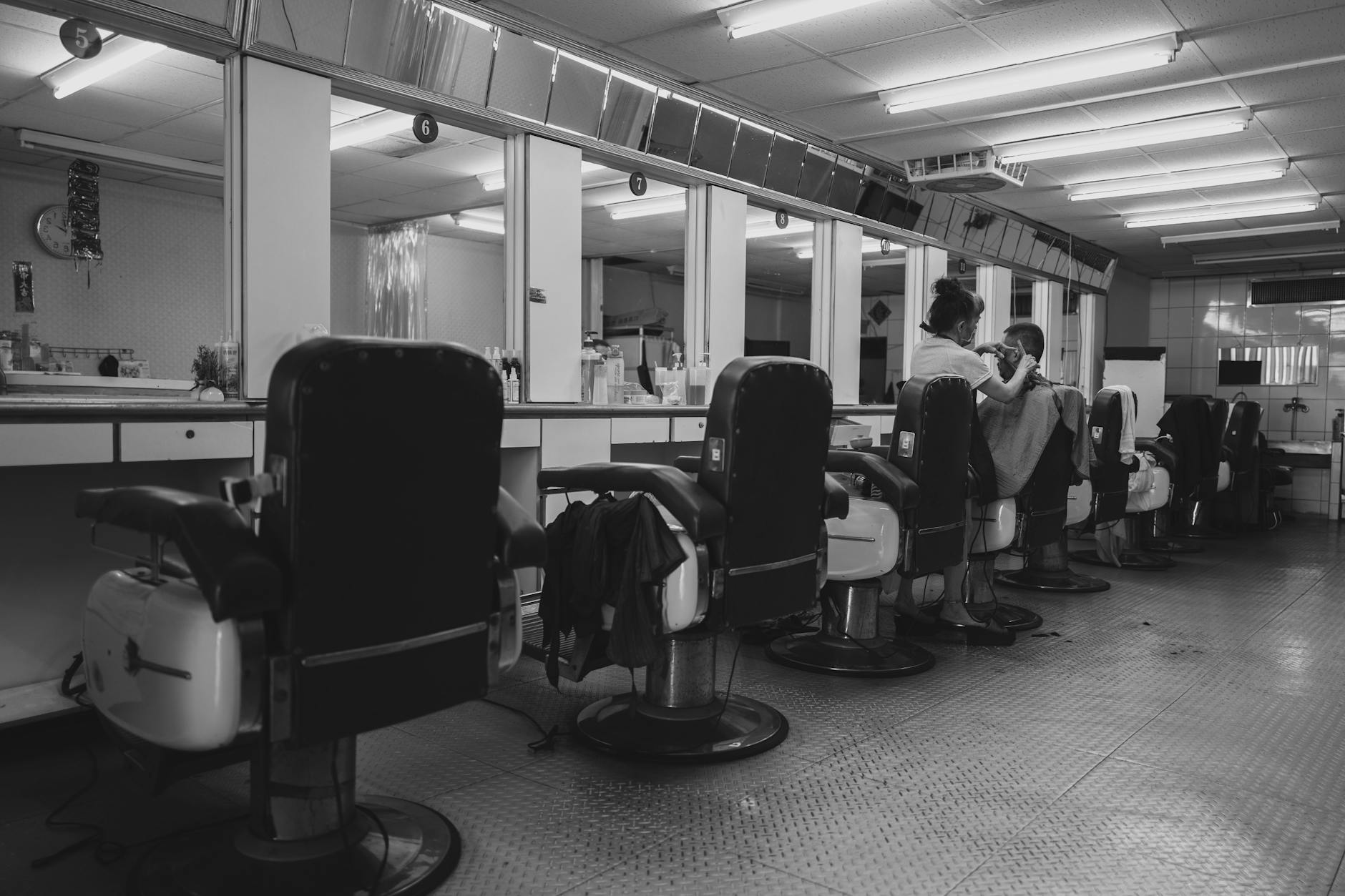 A black and white photo of a vintage barbershop with styling chairs and mirrors.