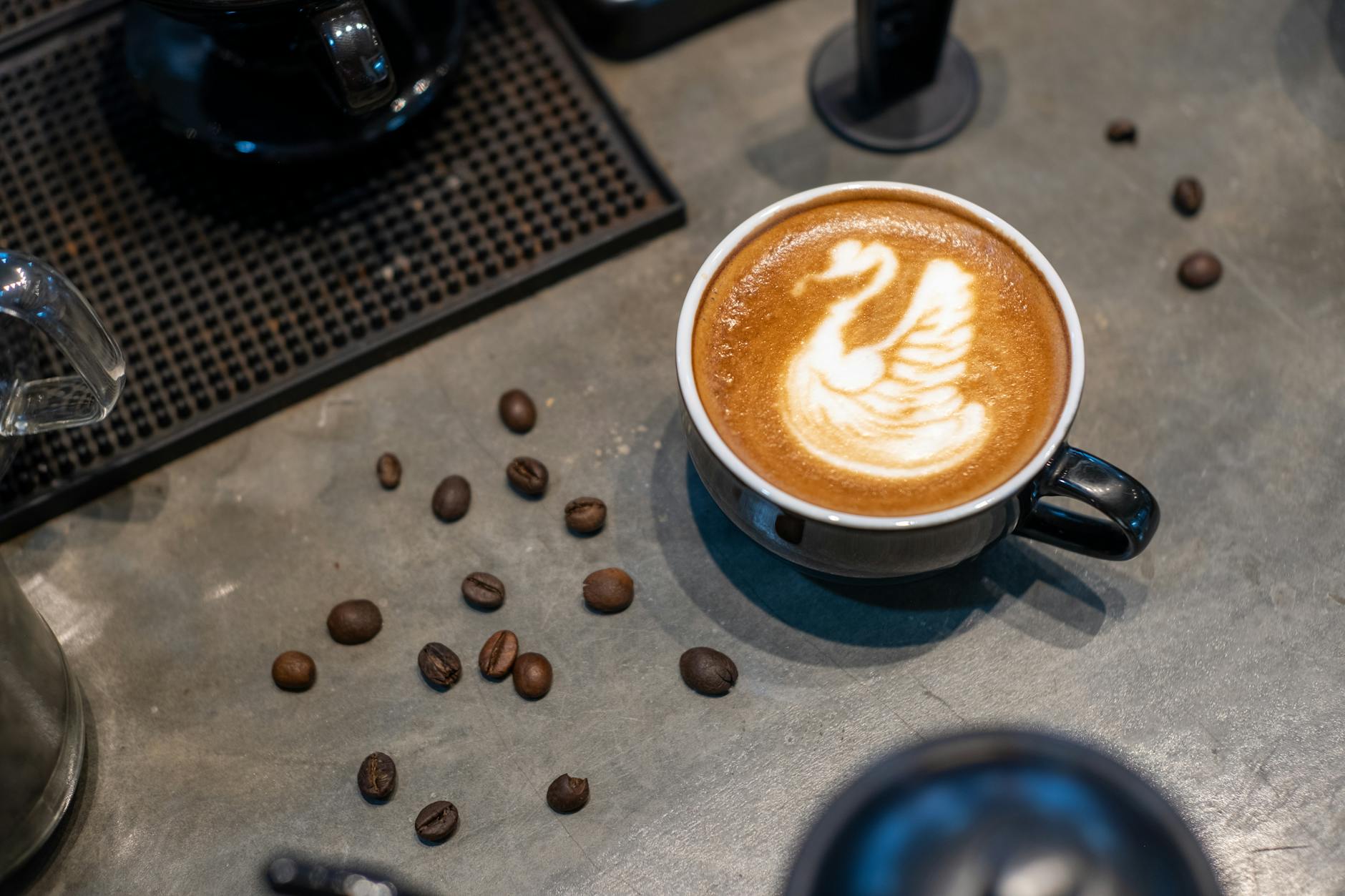 A beautifully crafted swan latte art in a black mug surrounded by coffee beans on a table.